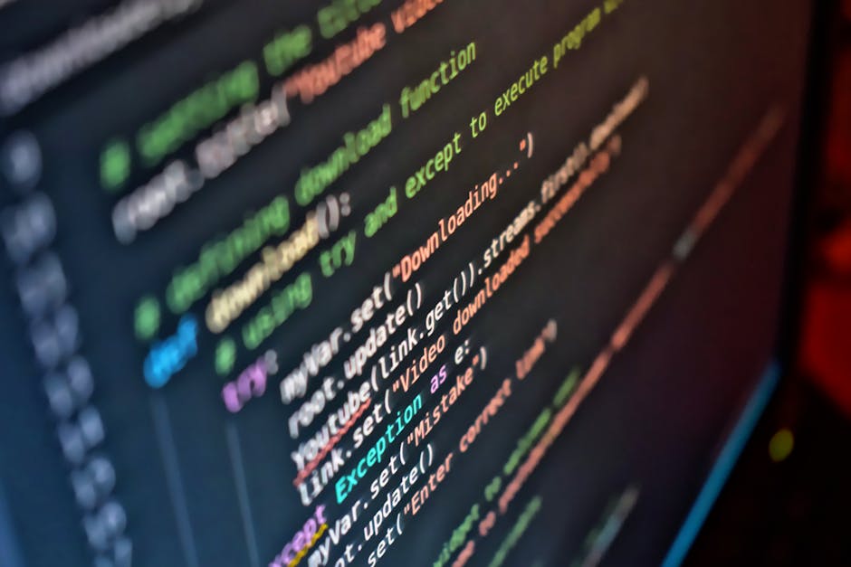 A close-up photograph of a computer screen displaying a coding interface with multicolored lines of code, including green, purple, orange, blue, and white text, representing a programming environment.